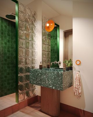 A green bathroom with a green terrazzo sink, a glass brick wall, and a green tiled shower
