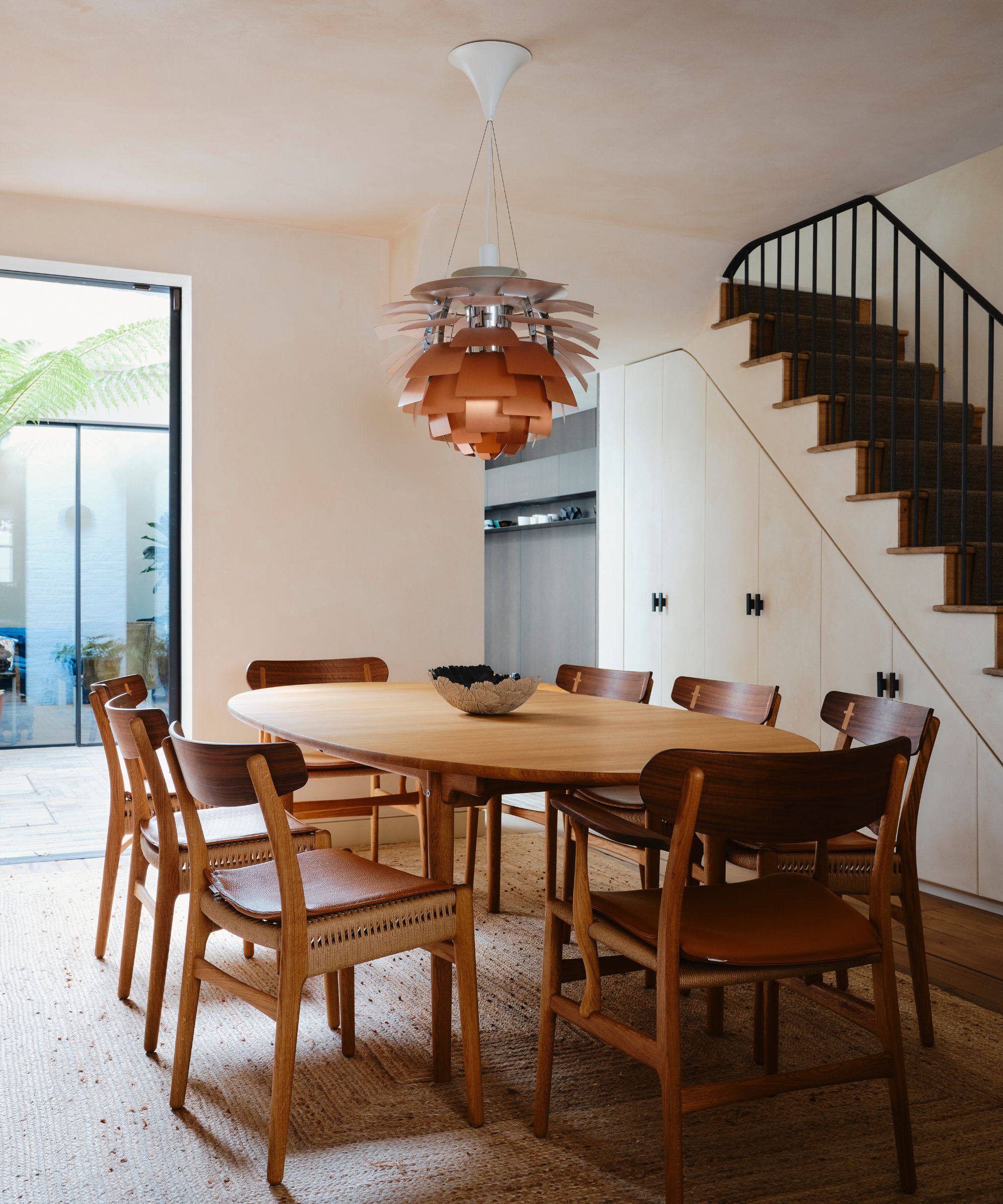 Modern dining room with plaster walls and large wooden table with statement silver and copper pendant light