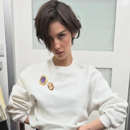 Gracie Abrams wearing a cream sweatshirt, red jeans, and white oxford flats