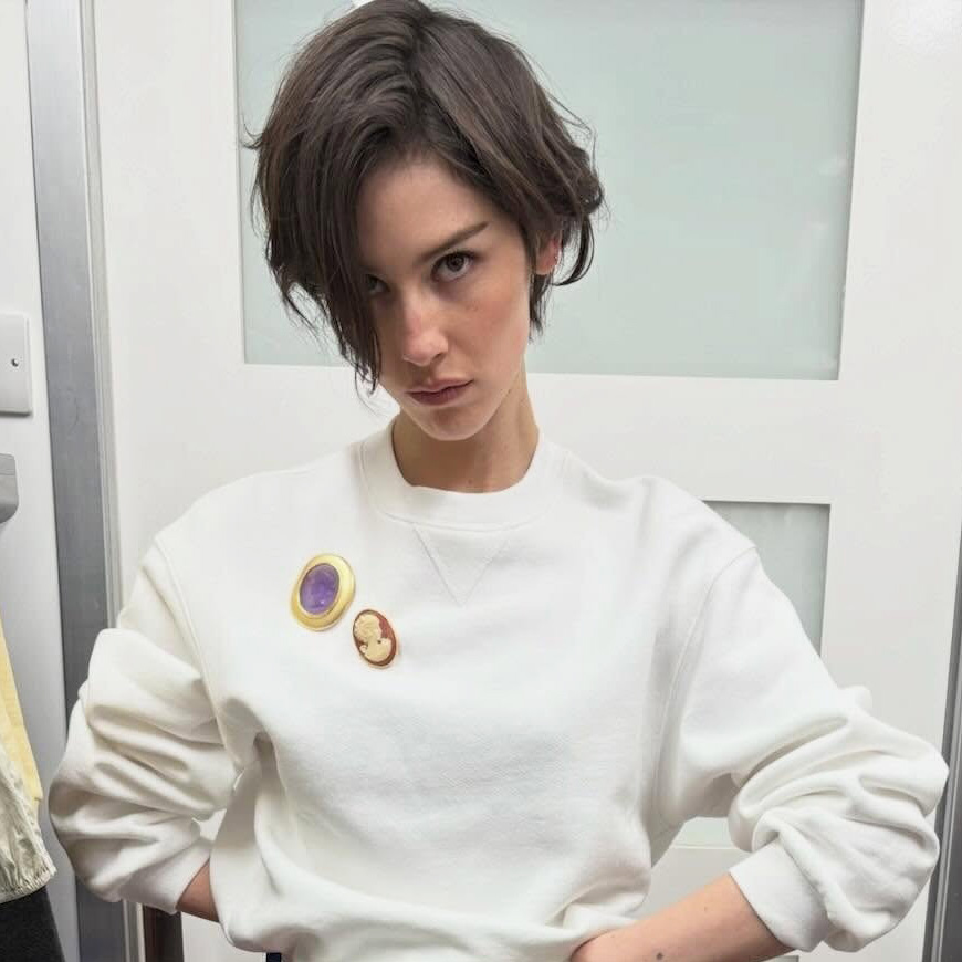 Gracie Abrams wearing a cream sweatshirt, red jeans, and white oxford flats