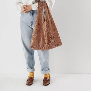 A person holding a brown printed reusable shopping bag 