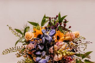 A beautiful bouquet of purple, yellow, pink and dark red flowers in front of a beige background.