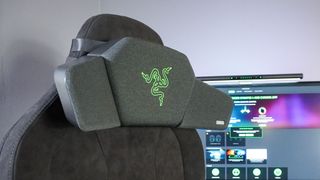 A gaming chair in front of a monitor with the Razer Clio wireless speaker head cushion attached to it