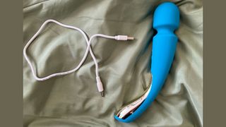Photograph of the LELO Smart Wand 2 on green satin next to USB charging cable