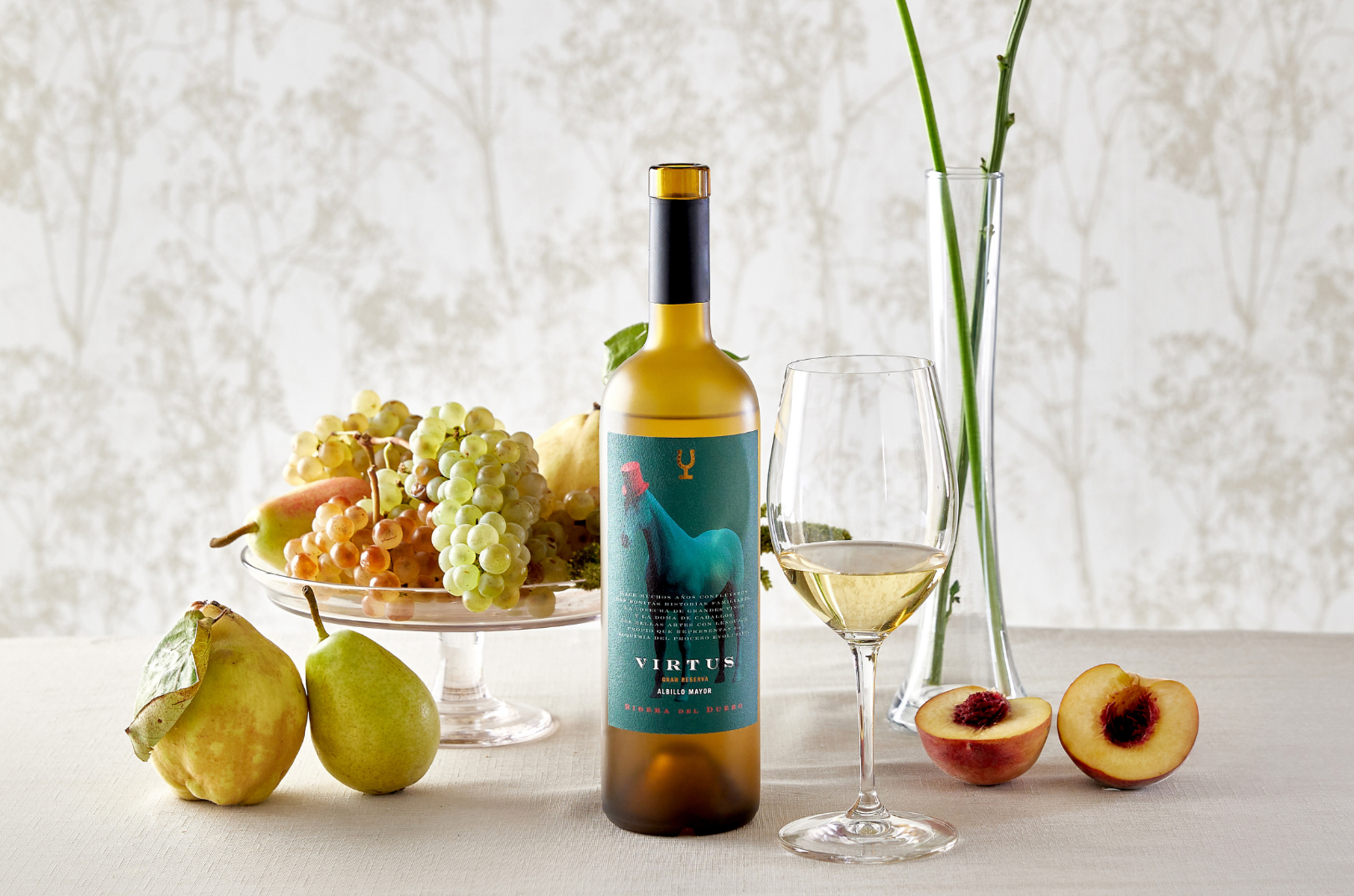 Bottle of Bodega Virtus white wine, with a glass next to it, and quince, a pear, nectarine and grapes