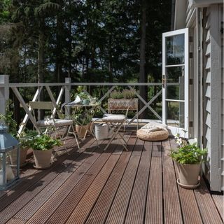 wooden decking with white railings, potted plants and bistro table and chairs