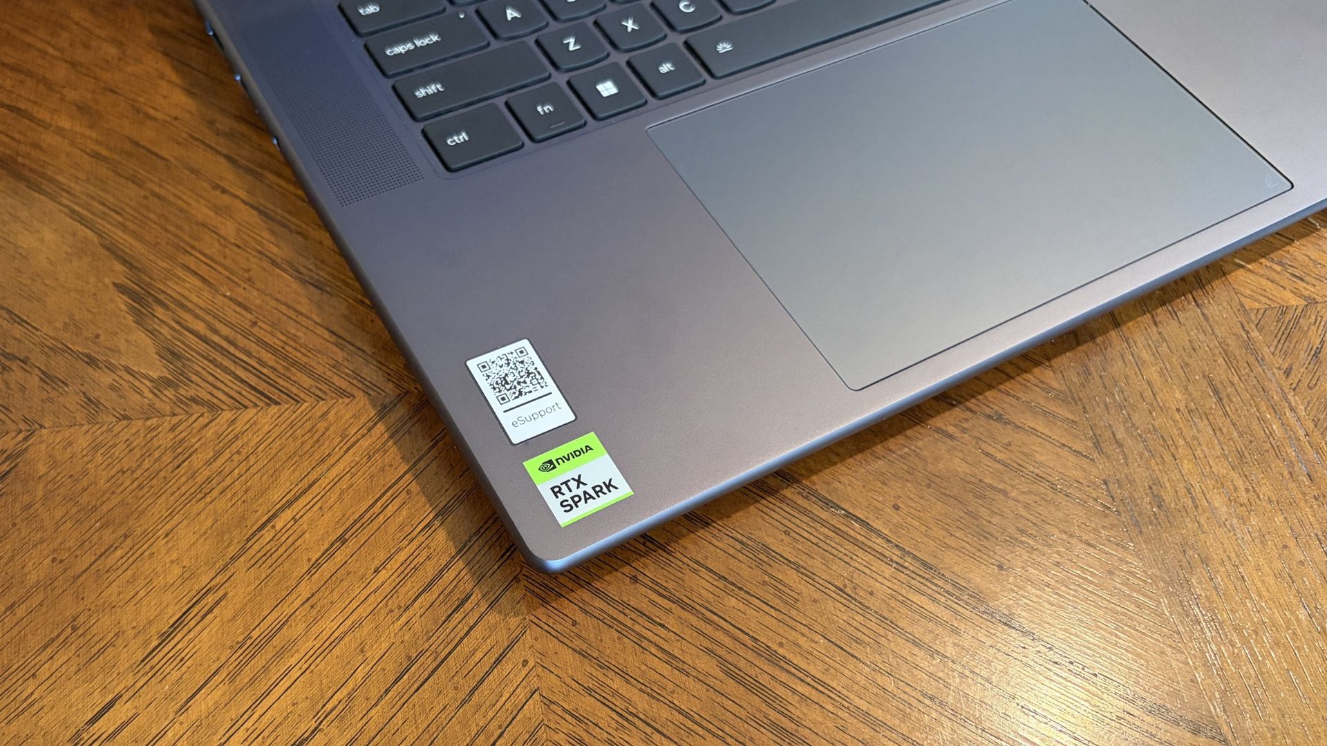 Close-up of a Lenovo Pro 9n’s keyboard and touchpad on a wooden desk, with a QR code and green RTX Spark sticker near the corner; practical, everyday scene.