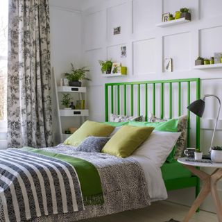 White bedroom with black and green accents. Green bedframe, panelled feature wall, black and white curtains and bedlinen.