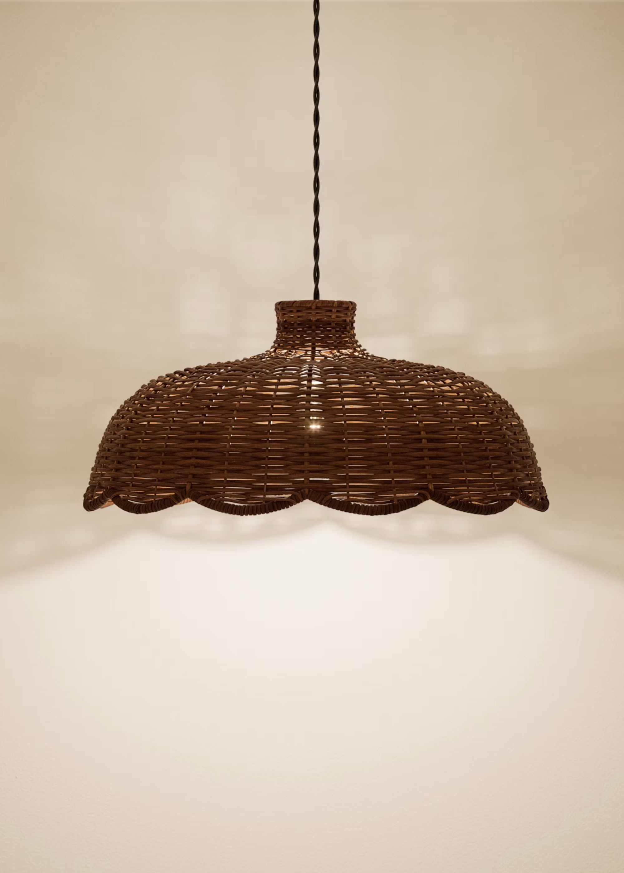 A rattan pendant light is dark brown against a wall