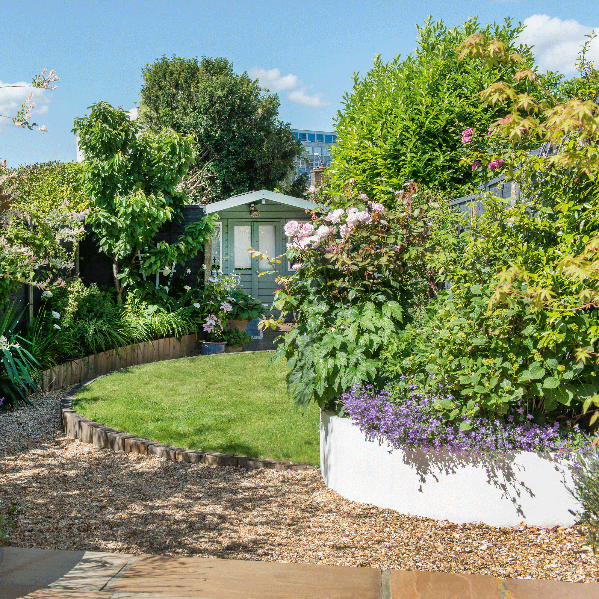 a garden with round raised beds and a curved lawn area with a painted green shed at the end
