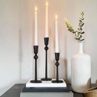 Three black candle holders of different heights next to a white sculptural vase