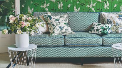 A living room covered in a green floral wallpaper with a patterned sofa and four floral-print cushions