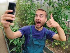 A man gives a thumbs up and takes a selfie in a garden