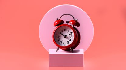 red alarm clock on pink and orange background 