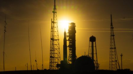 A silhouette of a rocket surrounded by scaffolding is seen in a dim yellow sunset
