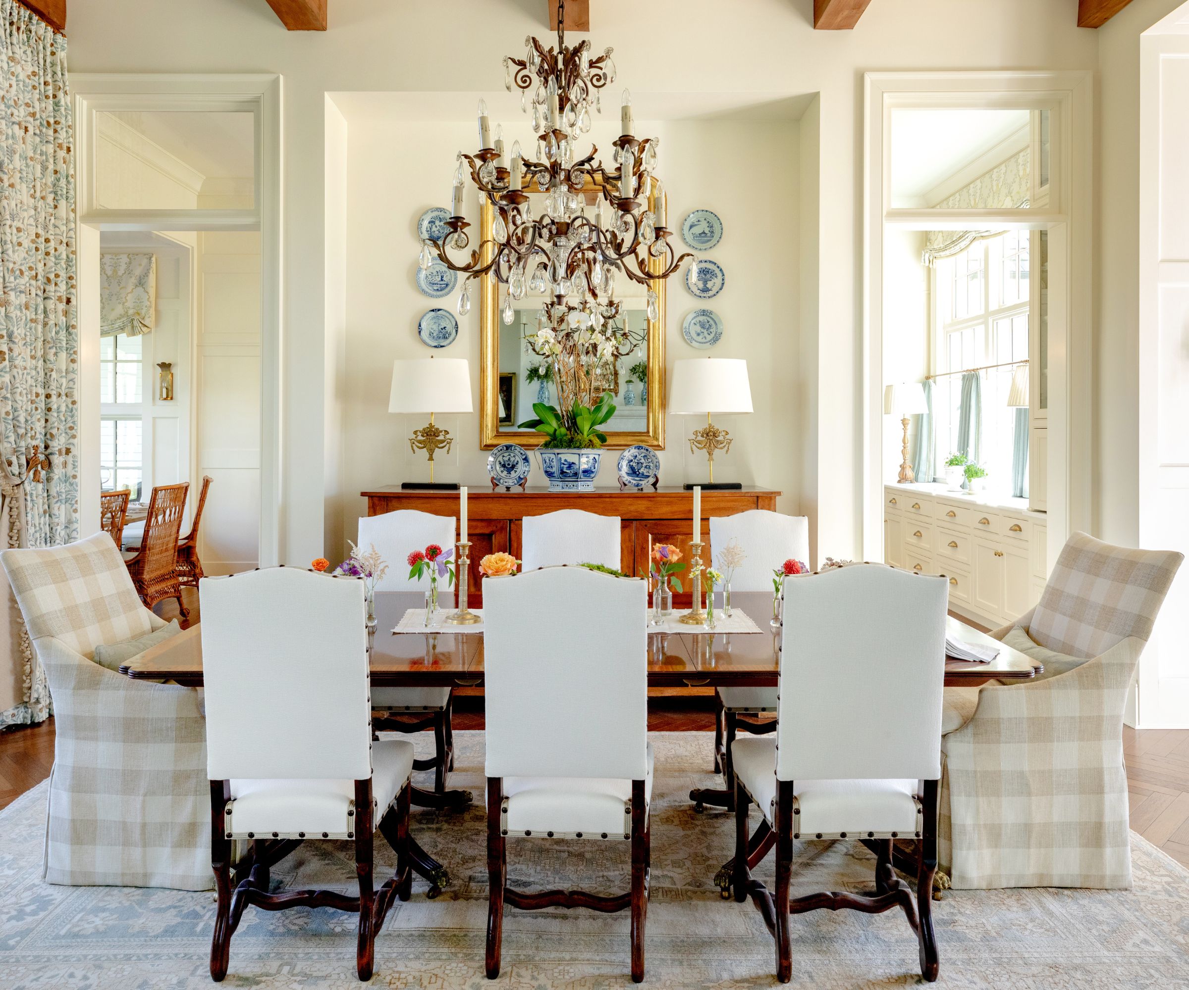 Dining room with wooden table, upholstered chairs, large gold mirror, chandelier and plates on wall