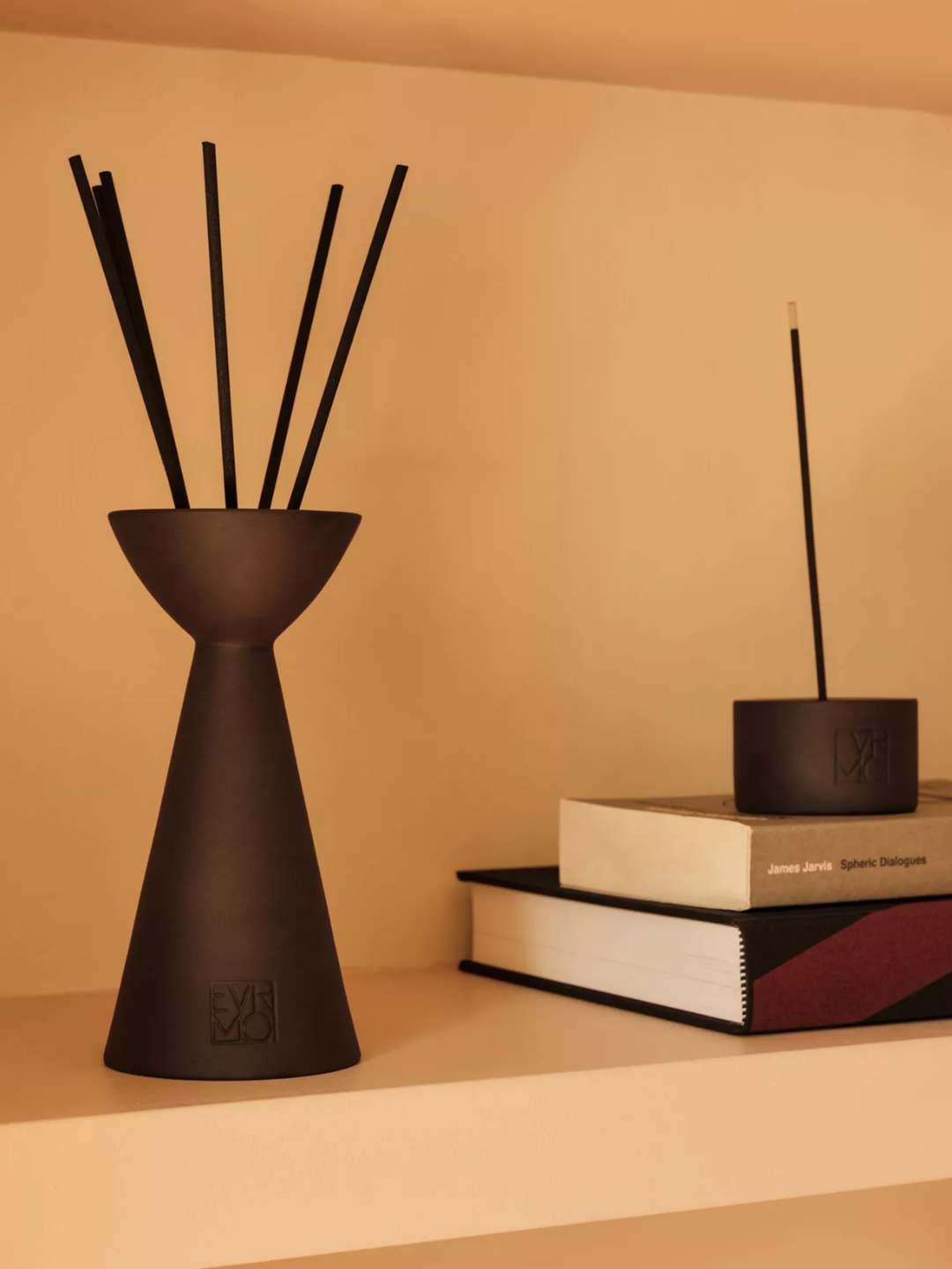 A black reed diffuser by a stack of books with an incense holder