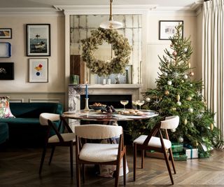 A neutral fining room decorated for the holidays with a large chirstmas tree and a wreath hung on the wall mirror