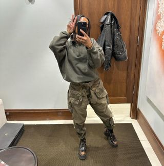 Telsha wearing an army green sweatshirt, cargo pants, and brown combat boots.