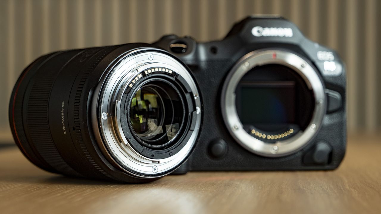 Canon RF 20mm F1.4L VCM lens on a wooden table, alongside the EOS R5 Mark II camera