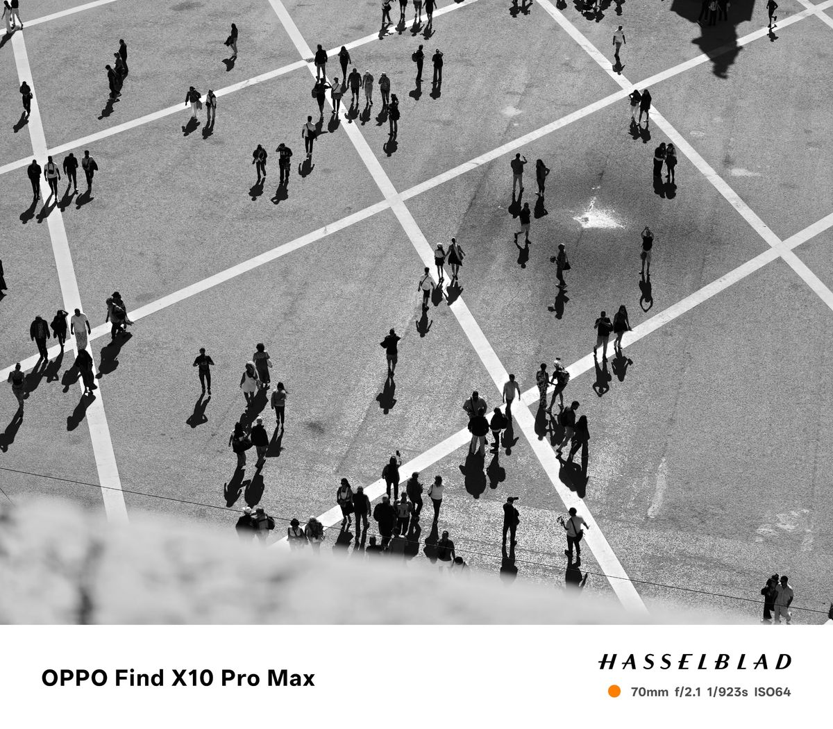 Black-and-white overhead view of people and long shadows crossing a geometric city square.