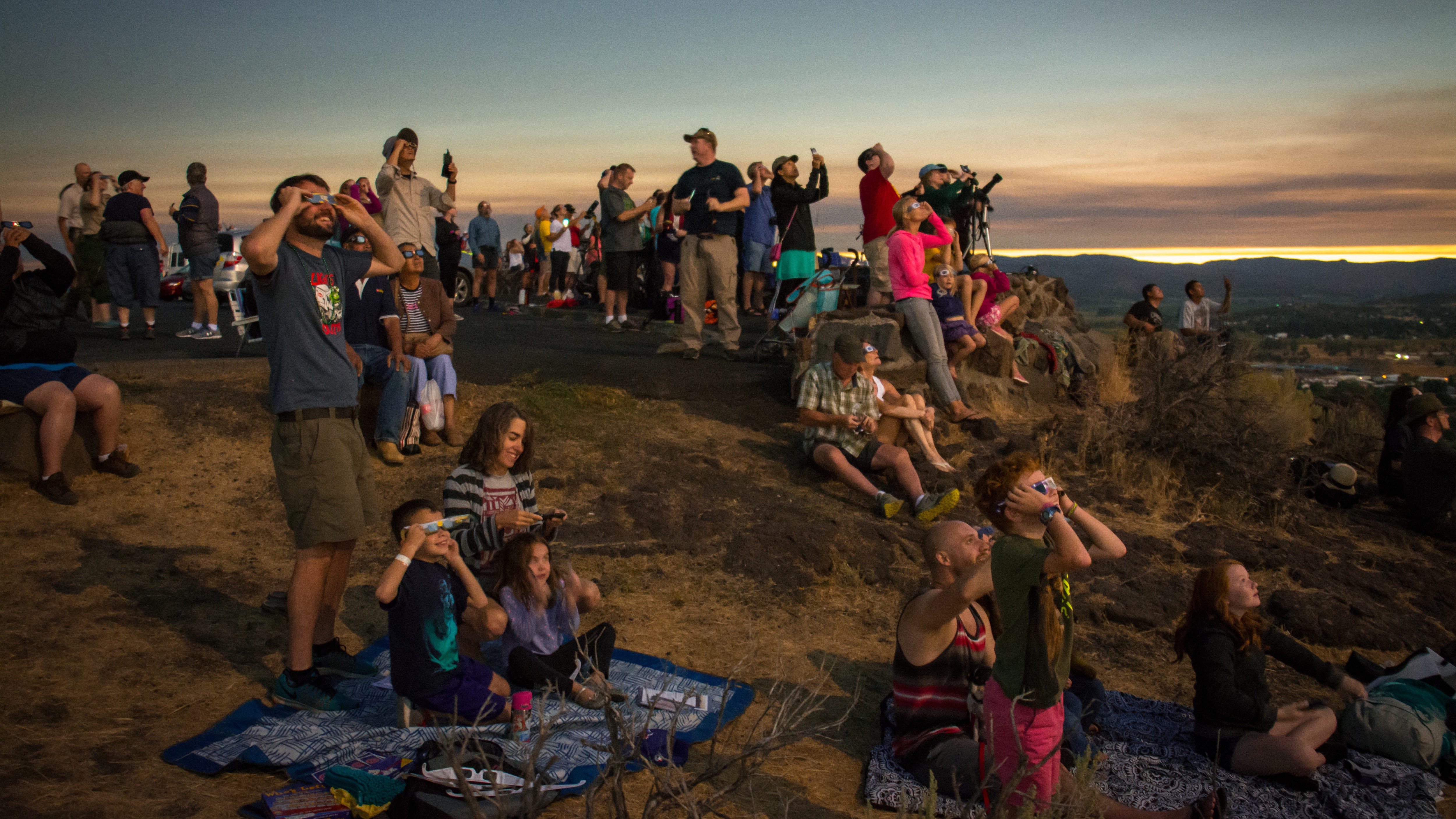 a group of people watch an ecilpse, there is an eerie light.