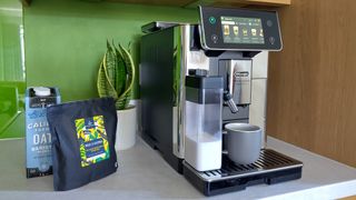 De'Longhi Primadonna Aromatic espresso machine on kitchen counter with coffee beans, oat milk, and snake plant