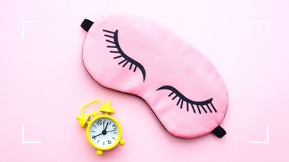 Pink sleep mask and yellow alarm clock over pink background