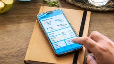 Smartphone showing daily nutrition goals. The phone is on a planner and a finger reaches towards the screen.