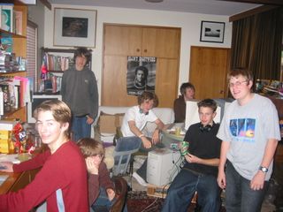 Seven teenagers pose in a room with computers, cables, and stacks of CD cases.