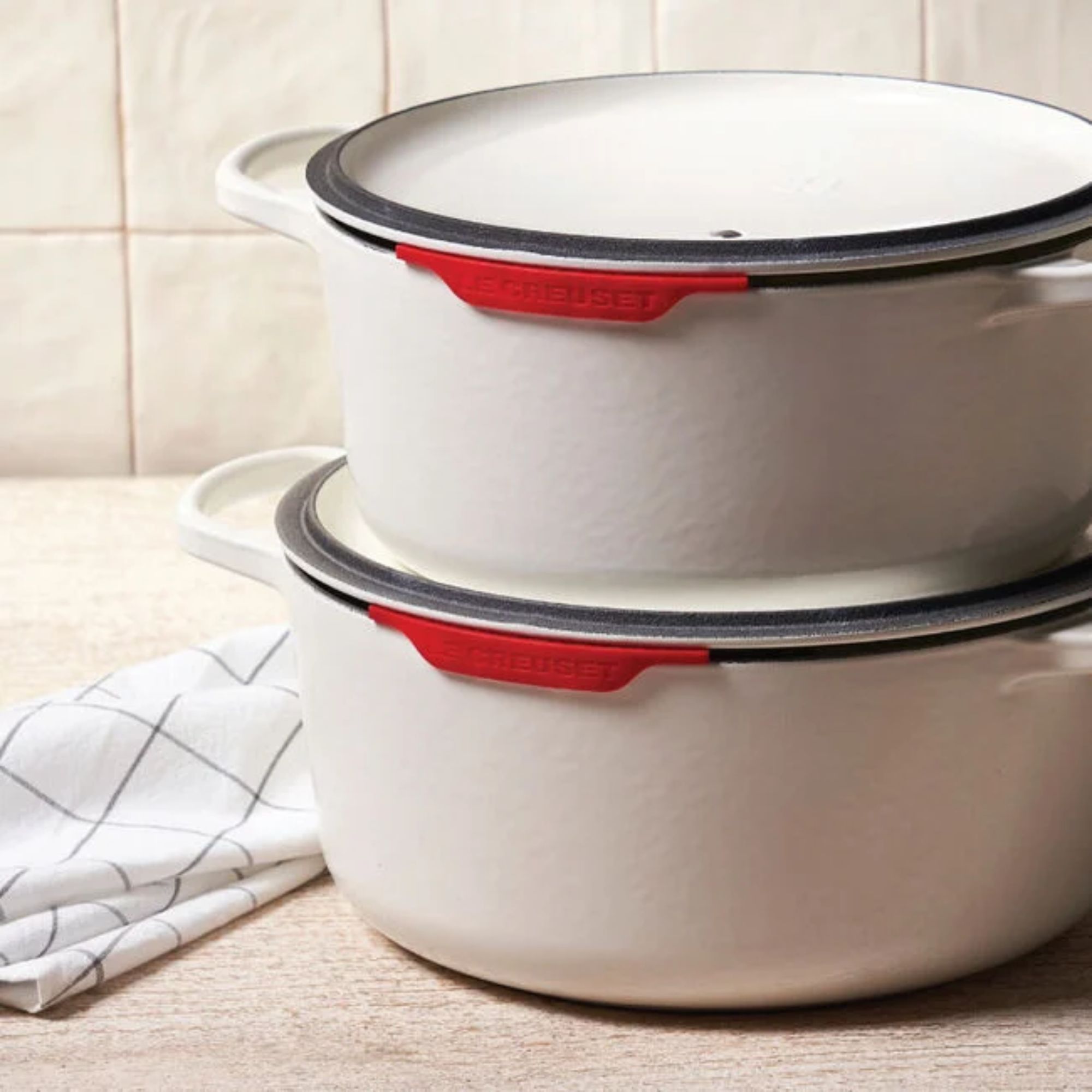 Two white pans with red pan lid protectors on the rims, stacked on top of one another