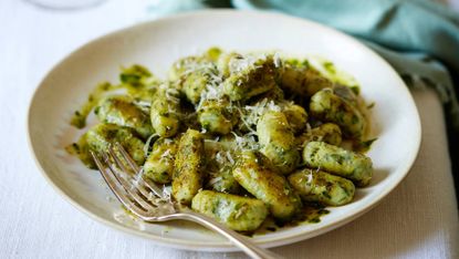 Bowl of gluten-free spinach gnocchi with a fork and fresh grated parmesan on top
