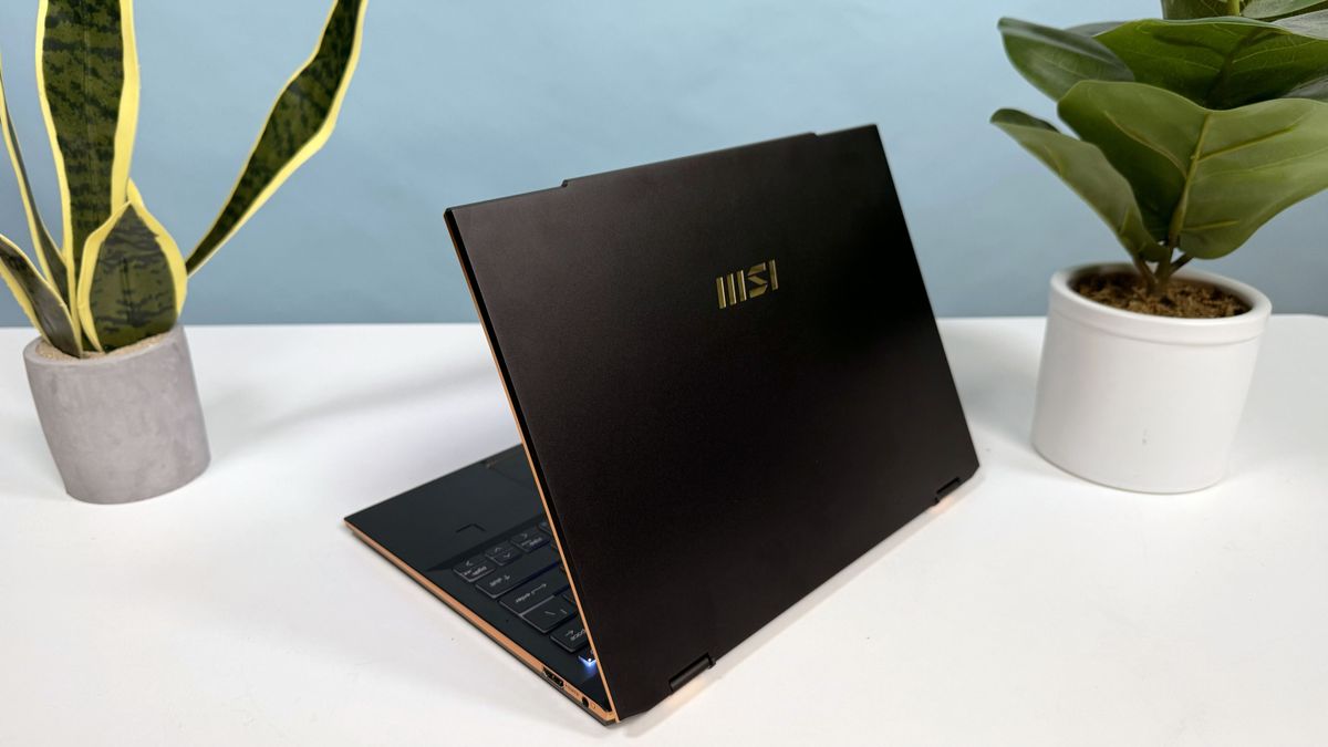 MSI Summit 13 AI+ Evo (A2VM) 2-in-1 laptop open in clamshell mode on a white table angled away to show the lid and MSI logo with two plants behind the laptop