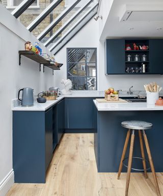 A kitchen with dark blue cabinets and white worktops with a sloped glass roof and an industrial style bar stool in front of an island