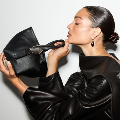 woman in a bun and black leather jacket looking at a black bag