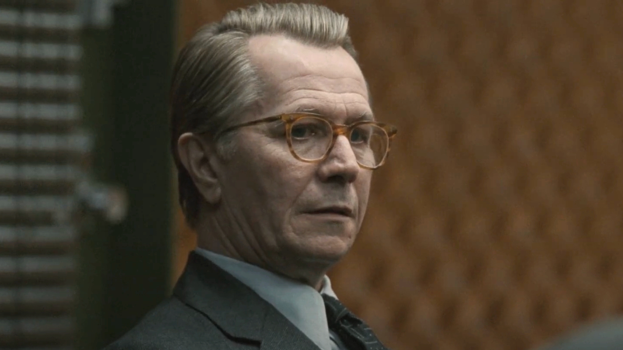 Gary Oldman sits with a look of concern in an orange walled room in Tinker Tailor Soldier Spy.