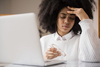Types of headache: Frustrated African American woman holding eyeglasses near laptop