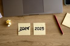 Note papers with text 2024 and 2025 on wooden work desk. Planning resolutions for New Year 2025. Laptop, eyeglasses, pen