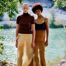 Two women wearing Prada tops and skirts standing in front of a lake