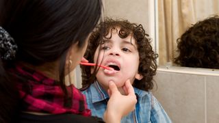 a mother brushes her young son's teeth