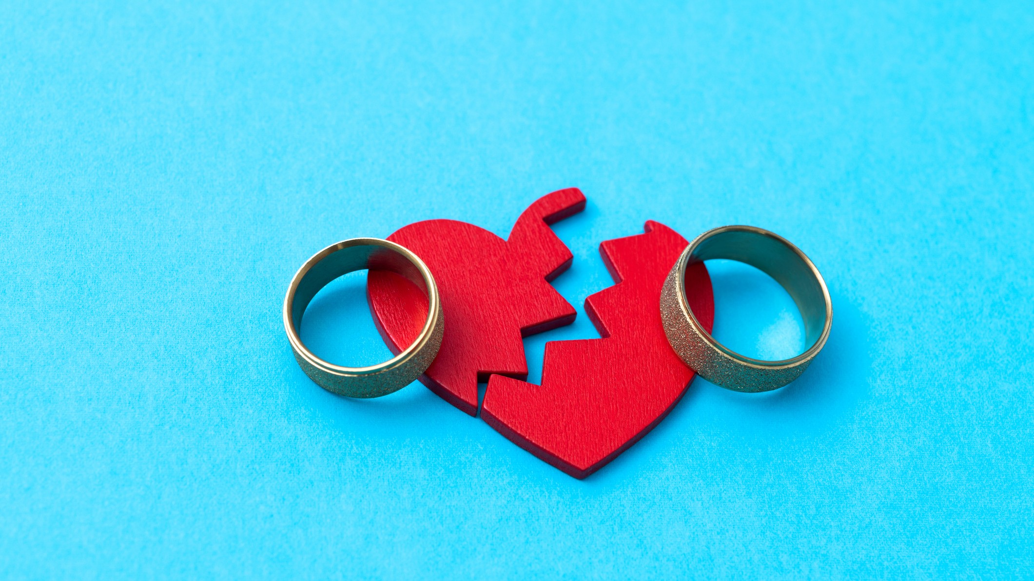 Wedding ring with broken heart on blue background - stock photo