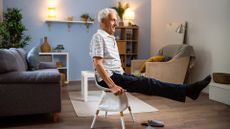 man in a striped tshirt sitting on a chair with legs outstretched with a living room setting behind him