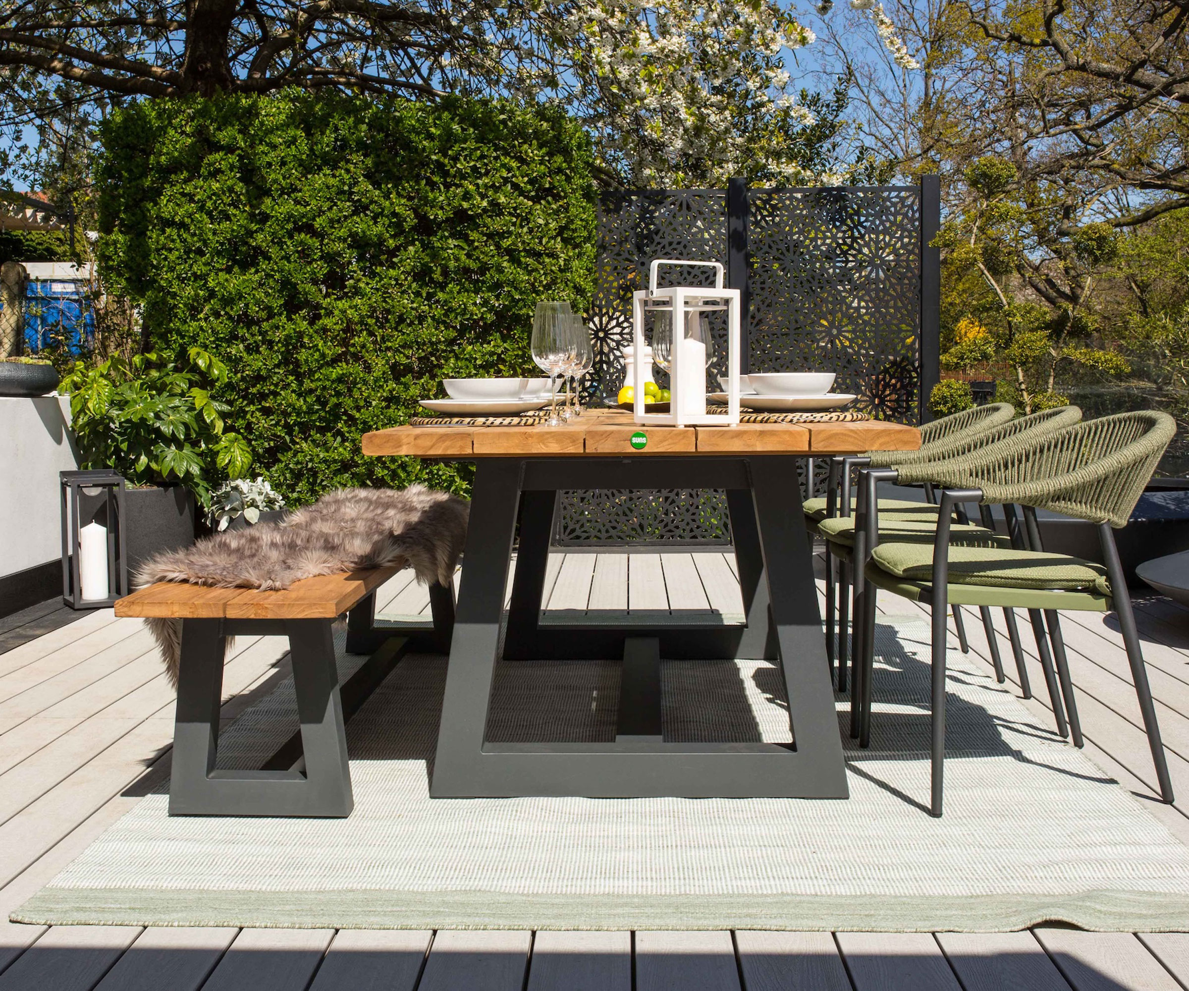 patio area with outdoor dining set and bench seat, chairs, lanterns, with trees in the background