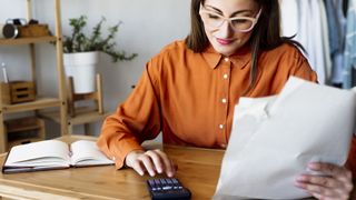 Woman holding paper looking at calculator