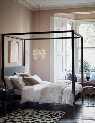 A four-poster black bed frame with bed, soft cushion decot and rug