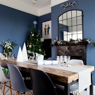 Blue dining room dressed for Christmas with blue dining chairs and arch mirror