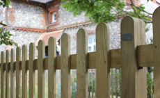 a wooden fence with one of the best fence stain options on it, outside a traditional brick house in the background, and a tree