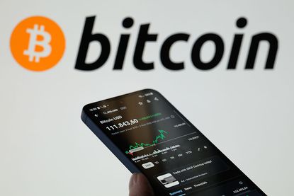 Bitcoin logo and phone looking at price of Bitcoin.
