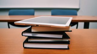 Tablet computer atop books on a classroom desk