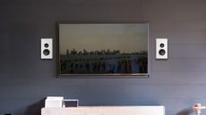 PSB PWM Sat speakers in white on a dark wall, either side of a wall-mounted TV